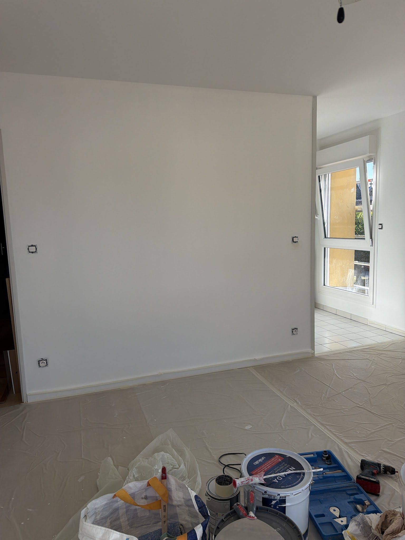 Sol bâché, pots de peinture et outils au pied d'un mur